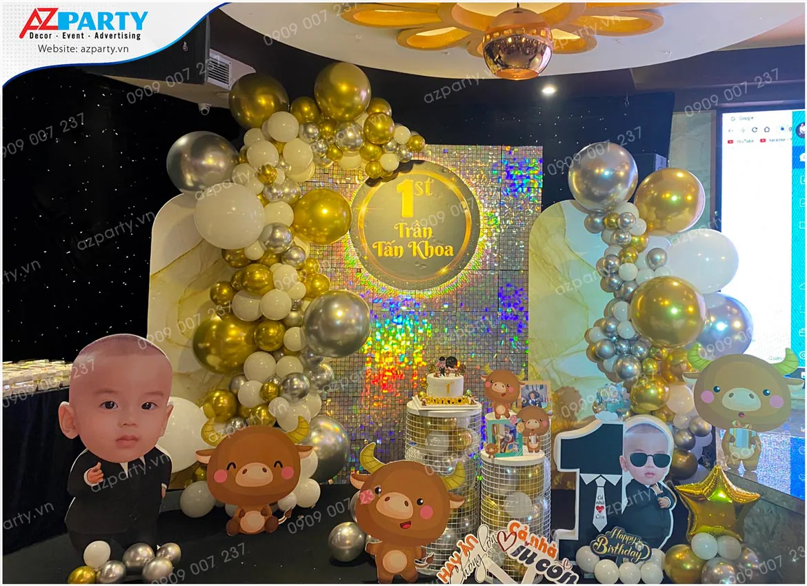 Trang trí thôi nôi tuổi Trâu cho bé Tấn Khoa với phông nền sequin lấp lánh phản chiếu ánh sáng cực đẹp, bong bóng màu vàng đồng và bạc.