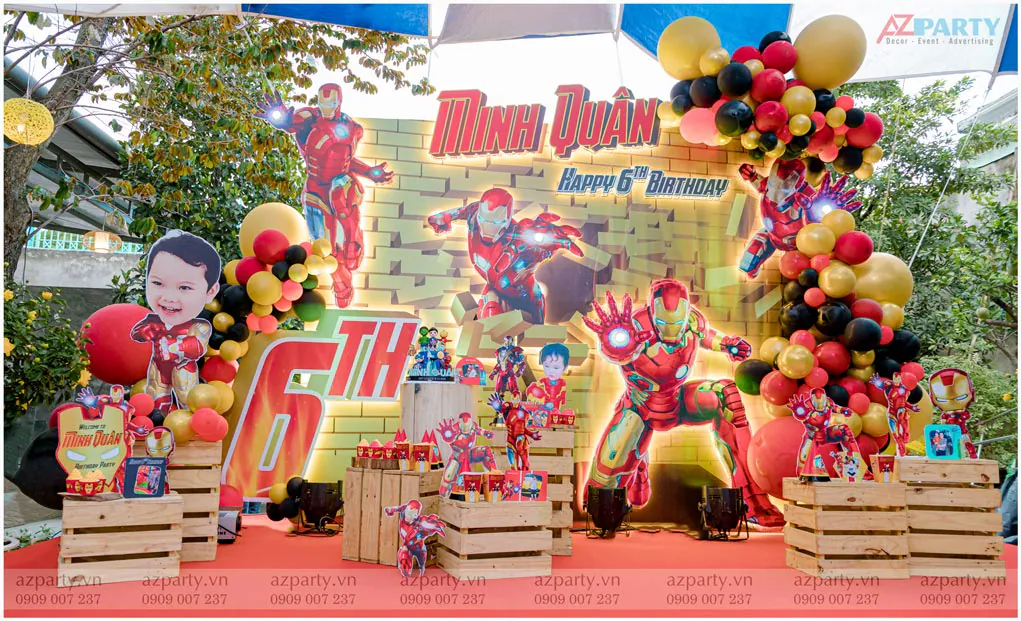 Sân khấu trang trí tiệc sinh nhật ngoài trời chủ đề siêu anh hùng Iron Man cho bé Minh Quân tròn 6 tuổi với các standee Người Sắt mạnh mẽ và cổng bong bóng đỏ vàng.