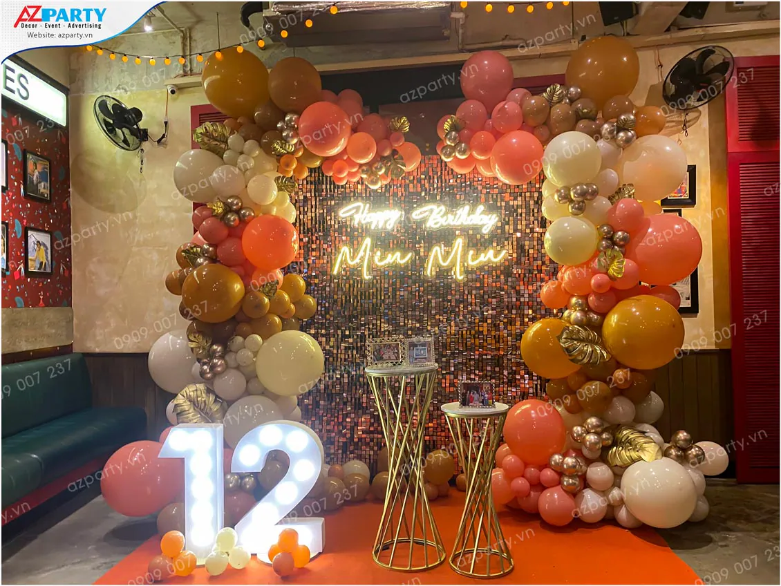 Trang trí tiệc sinh nhật Miu Miu tròn 12 tuổi với backdrop sequin vàng lấp lánh gắn chữ đèn neon và cổng bong bóng nghệ thuật màu pastel kết hợp bóng metallic chrome sang trọng.
