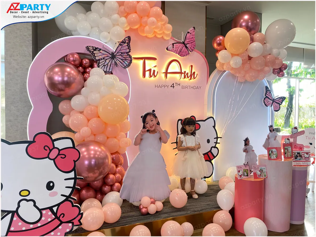 Bé Tú Anh cùng chị gái rạng rỡ tạo dáng chụp hình bên backdrop Hello Kitty sắc hồng pastel kết hợp các mô hình bướm bay xinh xắn.