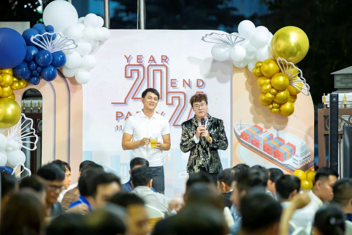 MC nam dẫn chương trình Year End Party 2024 của HVS Group giao lưu cùng một nam nhân viên đứng trước backdrop sân khấu vẽ hình tàu chở container.