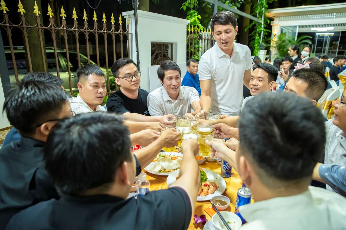 Nhóm nhân viên nam của HVS Group vui vẻ nâng ly bia chúc mừng tại bàn tiệc ngoài trời trong sự kiện tất niên của công ty.
