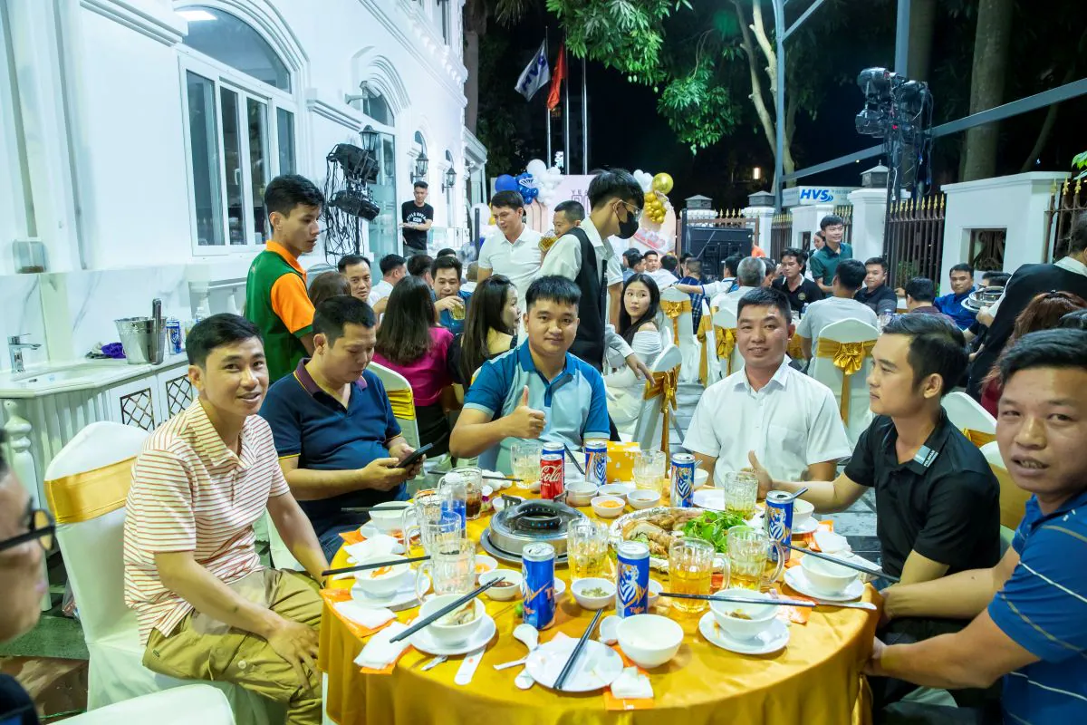 Các khách mời nam vui vẻ ngồi quanh bàn tiệc ngoài trời rộng rãi trong đêm tiệc tất niên HVS Group.