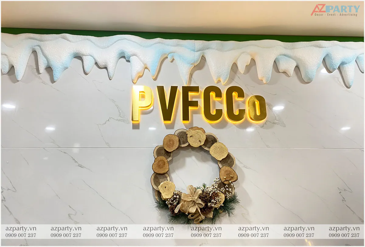 Một góc trang trí tường đá hoa cương với logo PVFCCo chữ vàng nổi bật, treo vòng nguyệt quế ghép từ các khoanh gỗ tròn tự nhiên và thạch nhũ băng giả sinh động