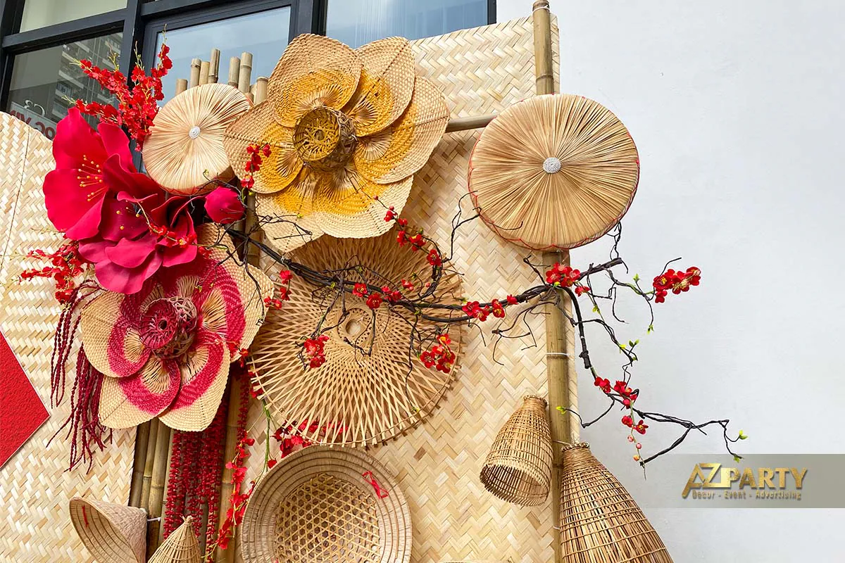 Chi tiết trang trí Tết với hoa tre đan thủ công, nón lá decor, cành mai đỏ và phông nền mây tre truyền thống