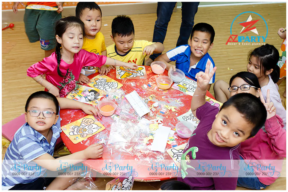 Các bé thiếu nhi hào hứng tự tay rắc cát màu rực rỡ lên tranh cát hoạt hình xung quanh bàn tròn tại sự kiện Tết thiếu nhi Apollo