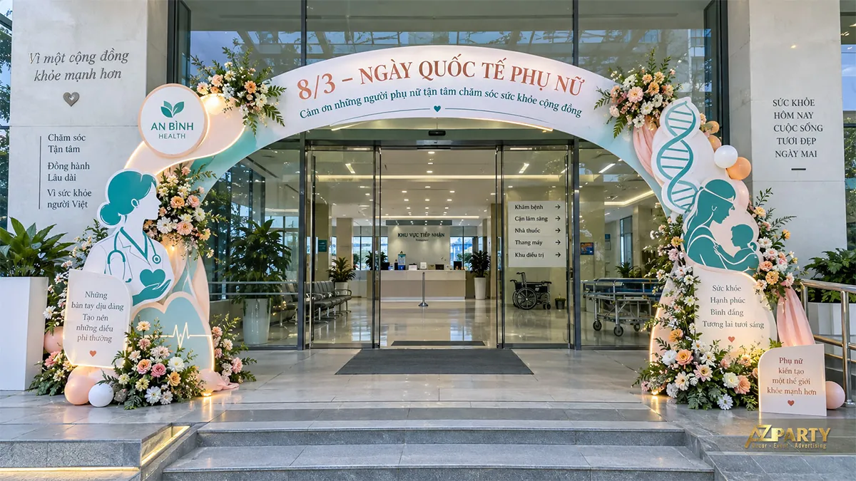 Cổng vòm xanh kem trước bệnh viện có hình nữ bác sĩ, mẹ bế con, chuỗi ADN và hoa ở hai chân cổng