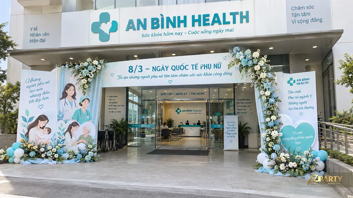 Cổng bệnh viện màu xanh trắng với hình phụ nữ chăm sóc người bệnh bên trái và hoa dọc trụ bên phải