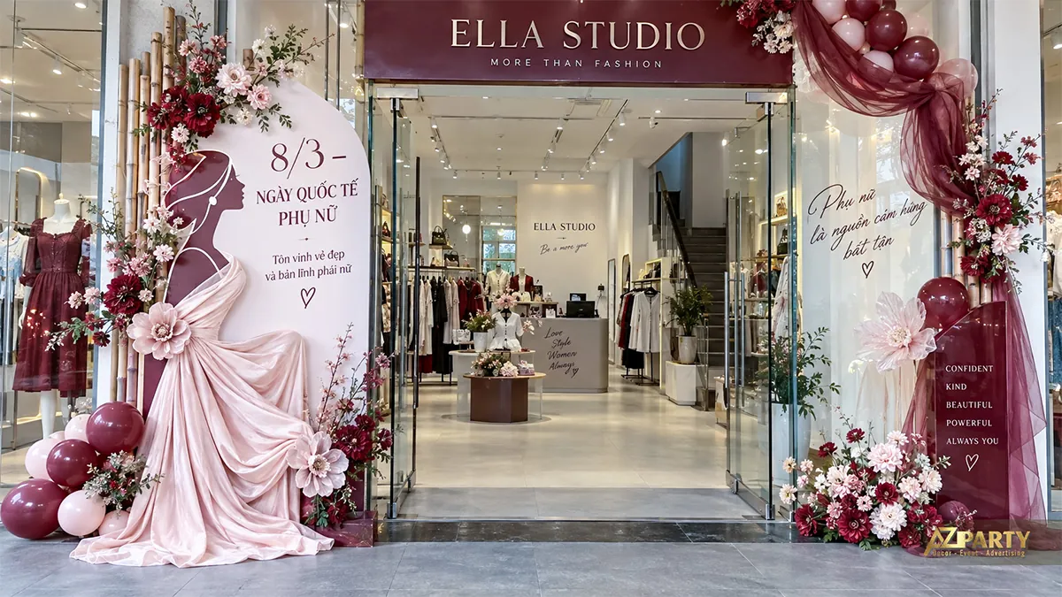 Lối vào shop thời trang với hình phụ nữ phối vải hồng bên trái, hoa và bóng đỏ rượu vang bên phải