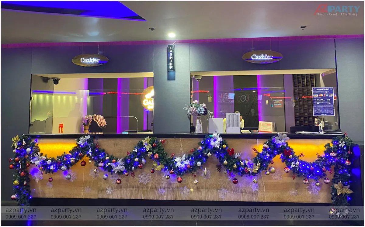 Trang trí Noel cho quầy thu ngân Galaxy Club bằng dải lá thông chăng đèn LED xanh dương rực rỡ kết hợp treo quả châu nhiều màu sắc dọc bàn quầy