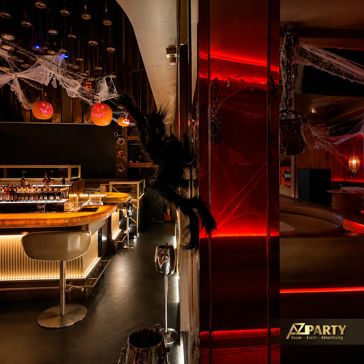 Góc nhìn dọc khu vực quầy bar với gương phản chiếu, ánh đèn đỏ và các vật trang trí Halloween treo phía trên.
