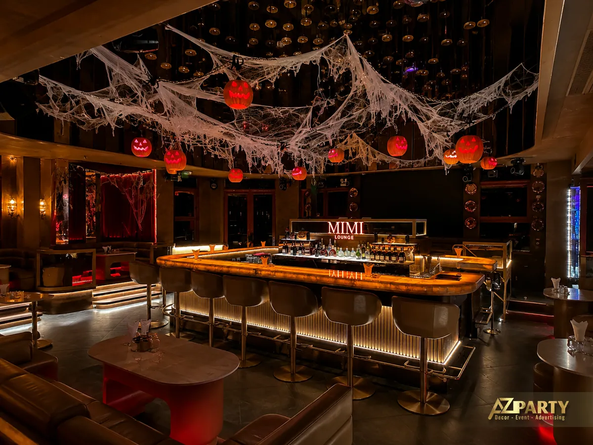Không gian quầy bar Mimi Lounge nhìn từ phía trước, nổi bật với mạng nhện trang trí, bí ngô phát sáng và ánh đèn vàng ấm.