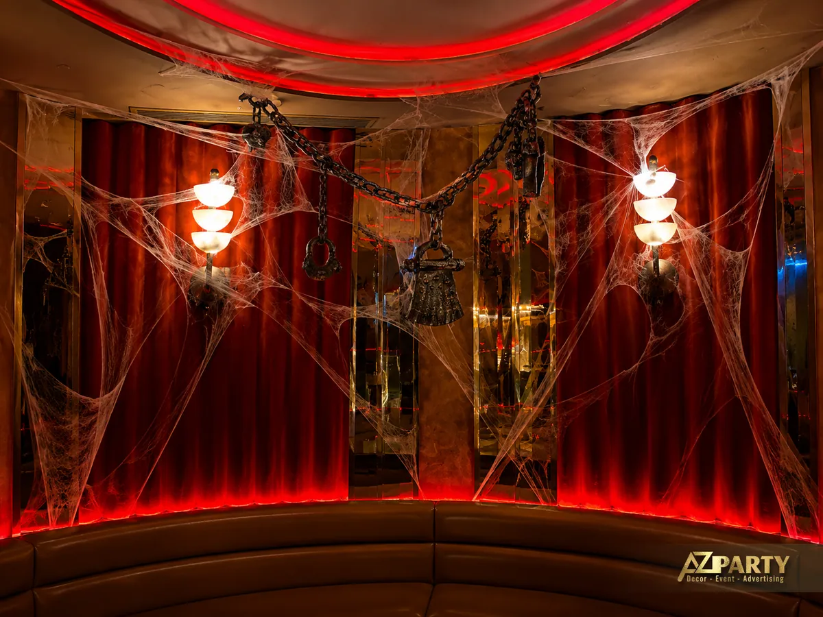 Mảng tường phía sau khu lounge với rèm đỏ, mạng nhện phủ trên khung trang trí và các đèn treo phát sáng.