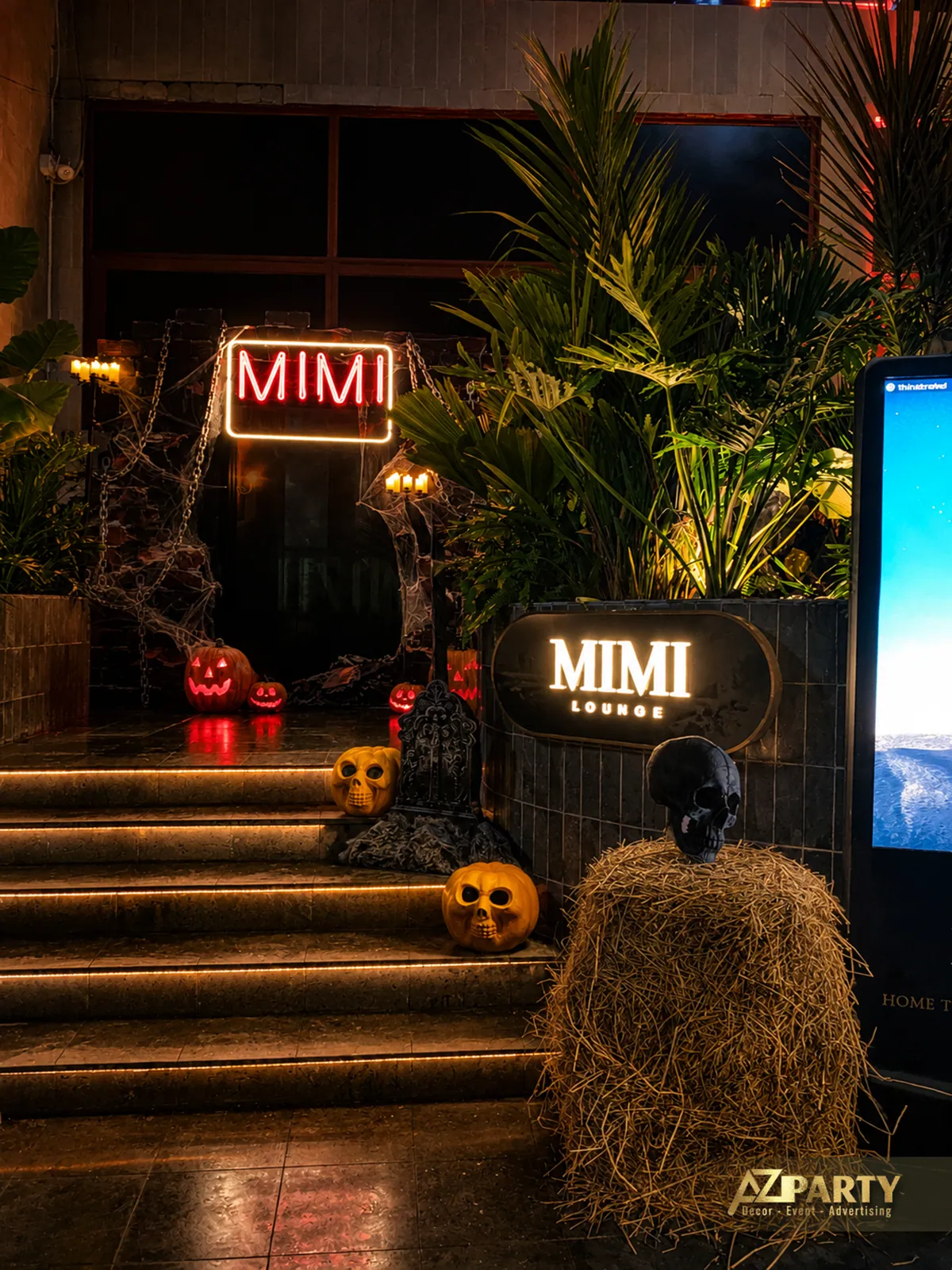 Lối bậc thang có cây xanh, bảng hiệu Mimi Lounge và các vật trang trí hình bí ngô đặt dọc khu vực đi lên.