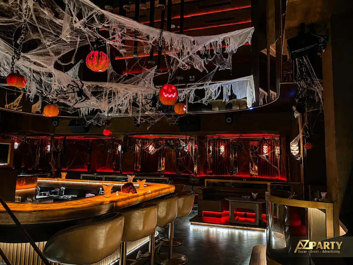 Góc nhìn rộng từ phía quầy bar, cho thấy ghế bar, mặt quầy, mạng nhện phủ trần và khu vực lounge phía sau.