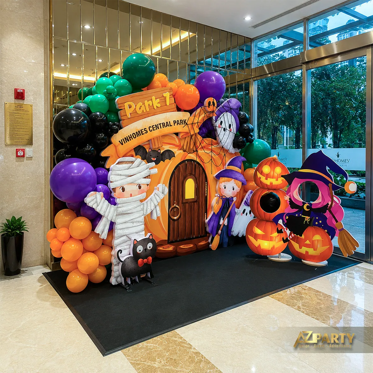 Góc rộng của khu check-in với khung vòm bóng bay cam tím, cửa gỗ, bí ngô và mascot.