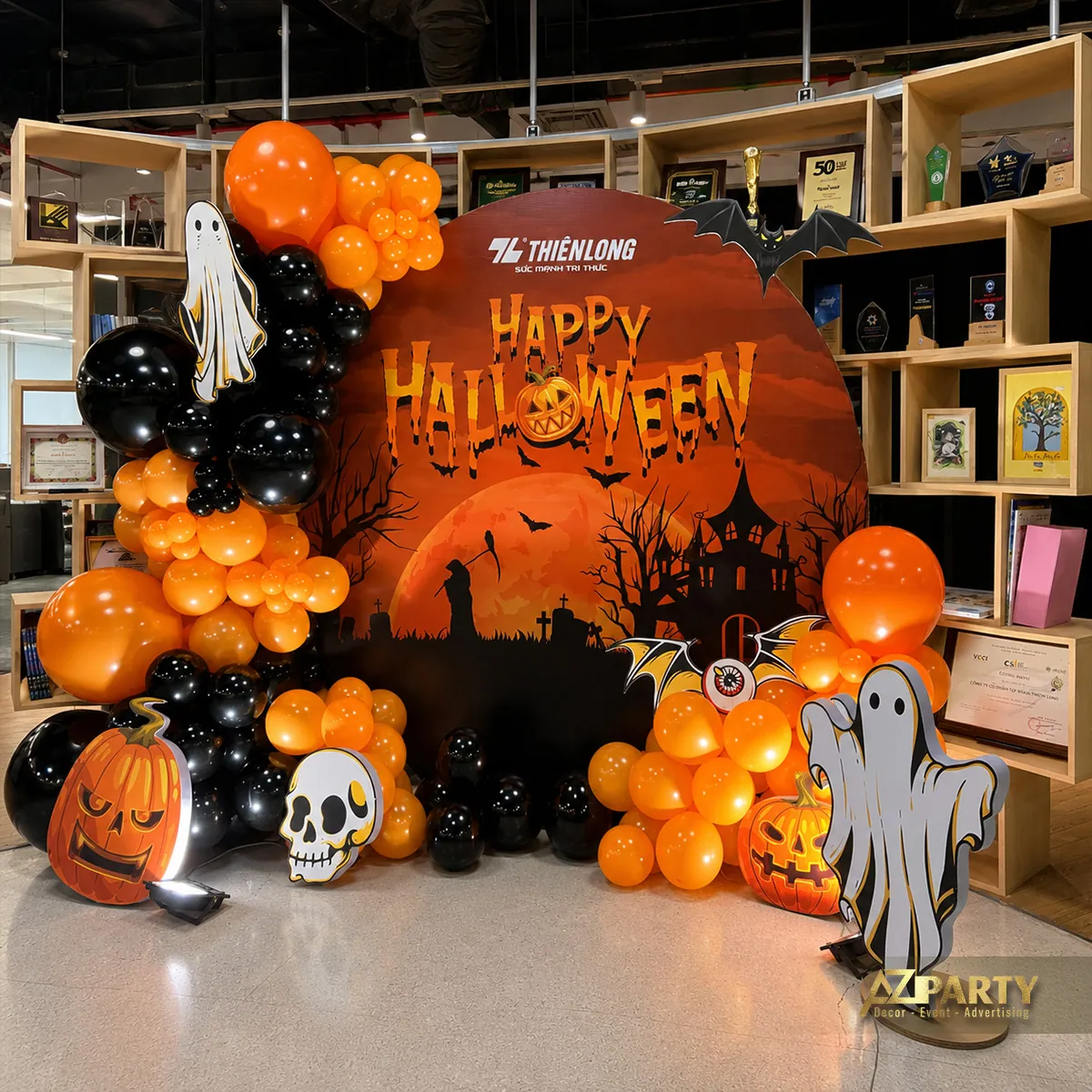 Góc chính diện với phông cảnh Halloween, bóng bay cam đen, các quả bí ngô và nhân vật ma trắng.