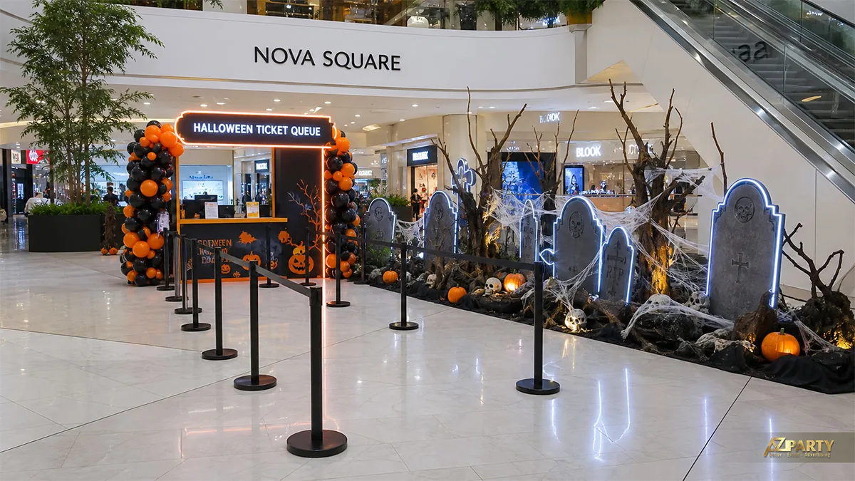 Khu xếp hàng Halloween bên thang cuốn với quầy vé, bia mộ viền sáng, cành khô và mạng nhện