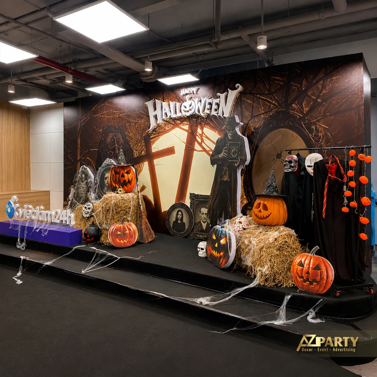 Toàn cảnh sân khấu trong không gian văn phòng, gồm backdrop Halloween, cụm bí ngô và các đạo cụ hai bên.