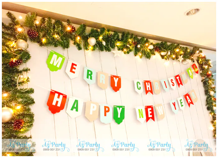 Cận cảnh dây cờ Merry Christmas và Happy New Year treo trên vách gỗ trắng kết hợp viền dây thông xanh đính quả châu và đèn led.