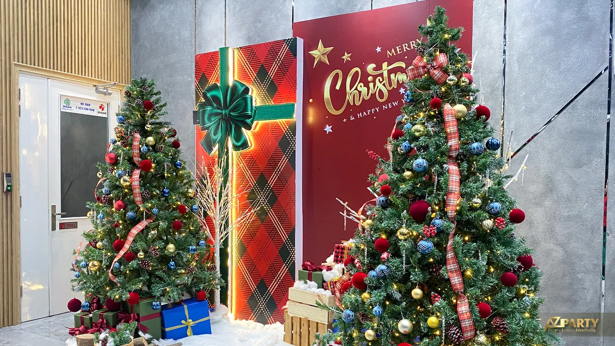 Hai cây thông Noel đặt cạnh phông nền đỏ và các hộp quà trang trí