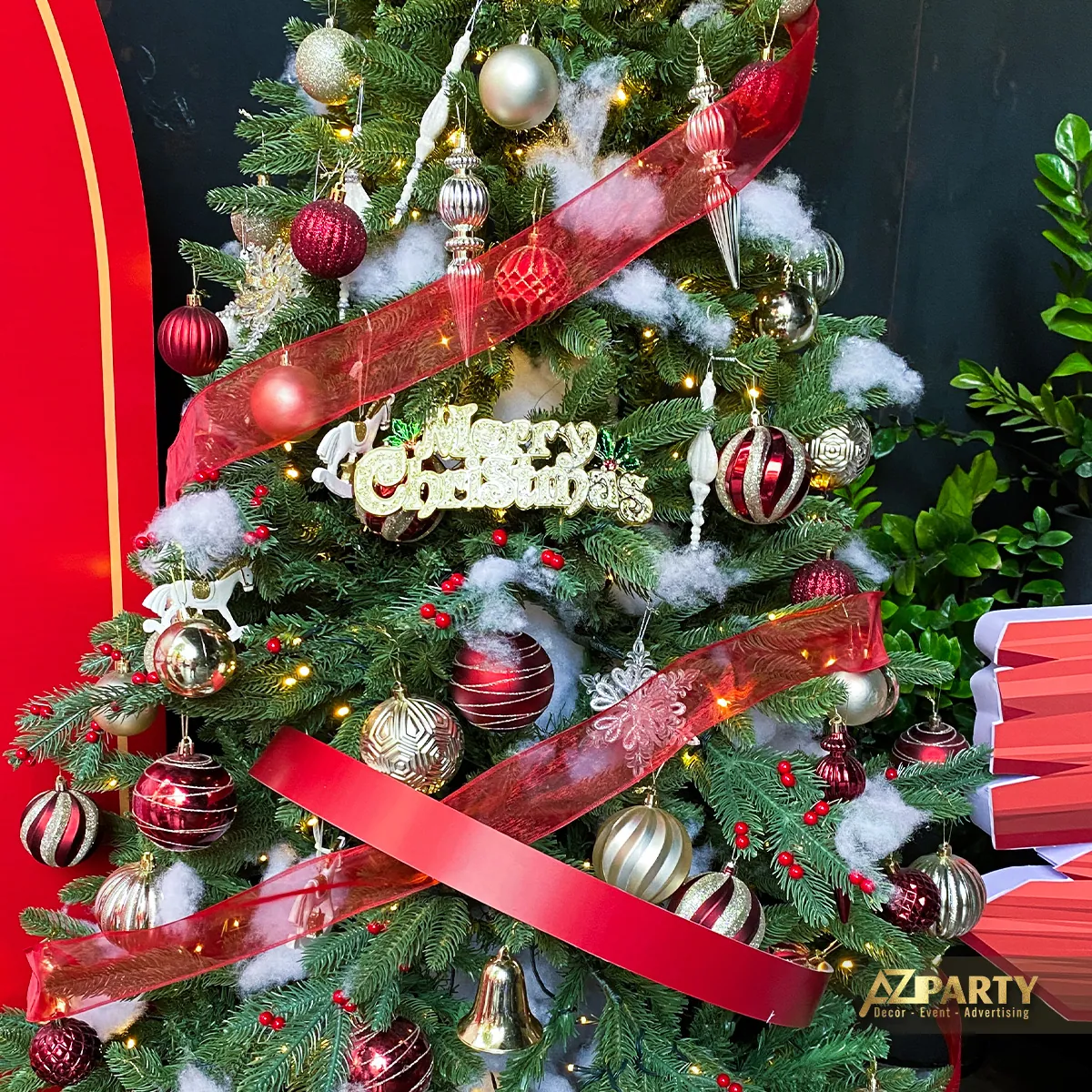 Cận cảnh cây thông Noel trang trí ruy băng đỏ, quả châu và chữ Merry Christmas