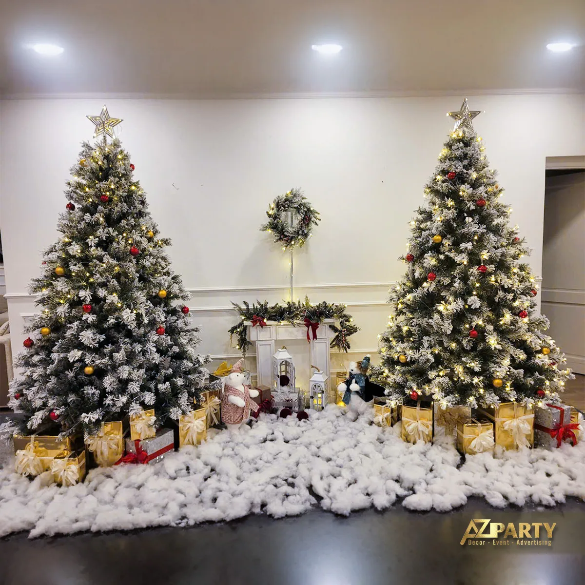 Hai cây thông phủ tuyết đặt cạnh lò sưởi và tiểu cảnh Noel trong phòng khách