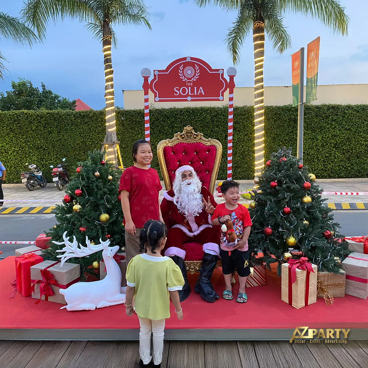 Cổng chụp ảnh Noel The Solia với ghế Santa, cây thông, hộp quà và gia đình đứng phía trước