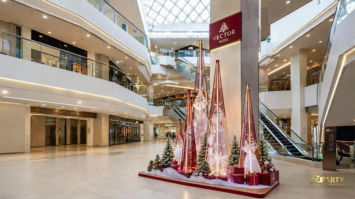 Tiểu cảnh Noel màu đỏ đồng với các cây thông hình nón, hộp quà và đèn treo giữa sảnh