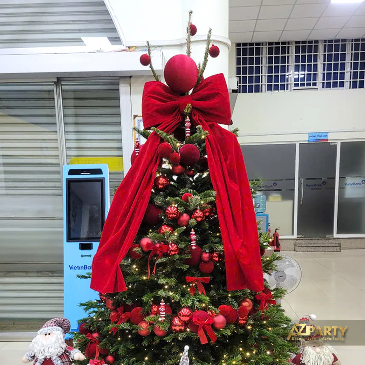 Góc nghiêng cây thông Noel lớn với dải vải đỏ, nơ và các hộp quà bên dưới