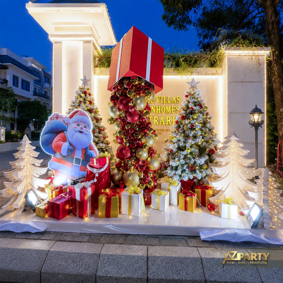 Toàn cảnh cụm trang trí Noel trước cổng với cây thông, hộp quà và nhân vật xanh
