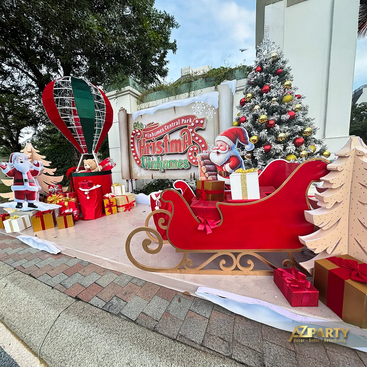 Góc chụp xiên cụm Noel với xe trượt tuyết màu đỏ, Santa, cây thông và khinh khí cầu