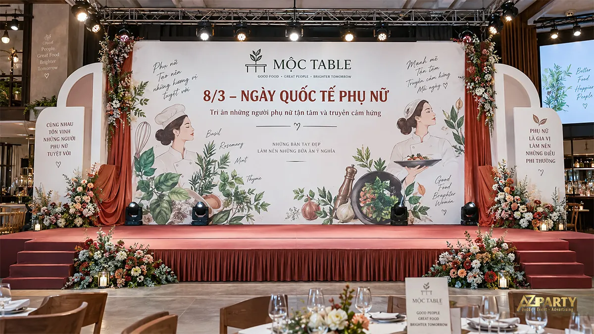 Phông nền phụ nữ làm bếp và họa tiết rau thơm, rèm cam đất hai bên cùng hai lối lên sân khấu