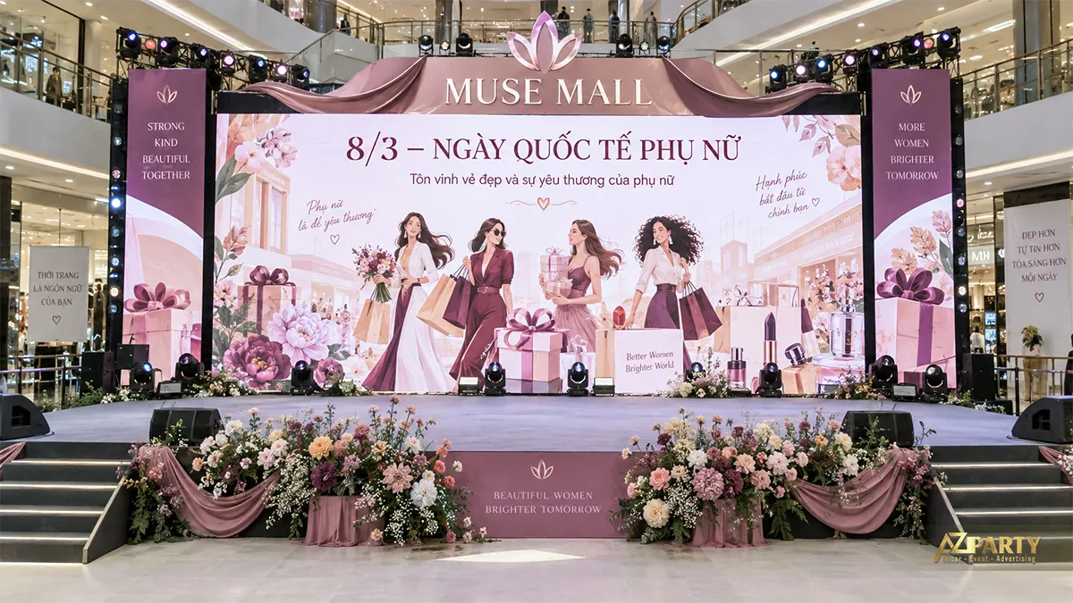 Sân khấu hồng đỏ trong sảnh trung tâm thương mại với hình phụ nữ mua sắm và cụm hoa ở hai đầu