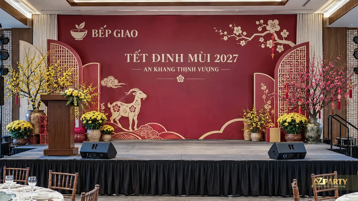 Sân khấu phông đỏ mận với vách lưới, bục phát biểu, hoa mai và hoa đào
