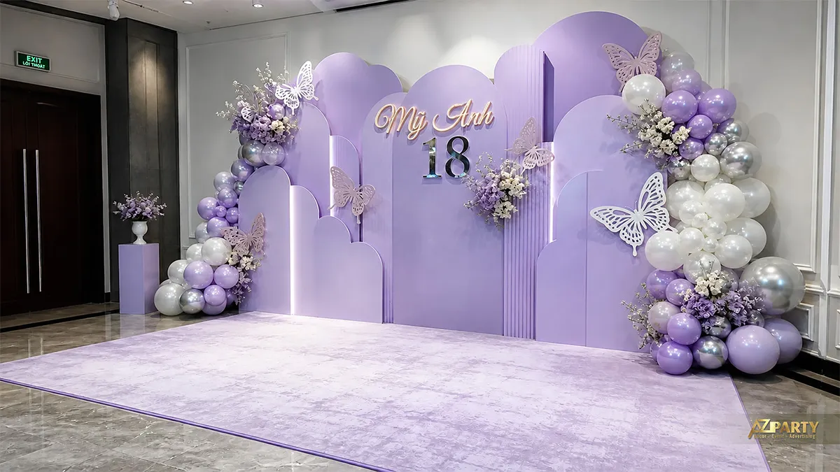 Backdrop sinh nhật 18 tuổi cho Mỹ Anh tông tím lavender, phối bướm, hoa và bóng trắng bạc.