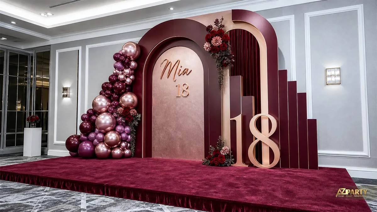 Sân khấu sinh nhật 18 tuổi cho Mia tông burgundy, phối hoa đỏ, bóng ánh kim và số 18.