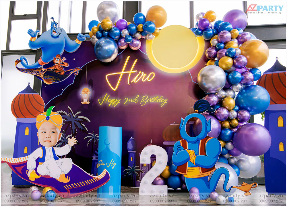 Cận cảnh khu vực trung tâm sân khấu với chữ đèn LED 'Hiro Happy 2nd Birthday', mô hình Thần Đèn Genie khoét mặt để chụp ảnh và bong bóng nhiều màu sắc.