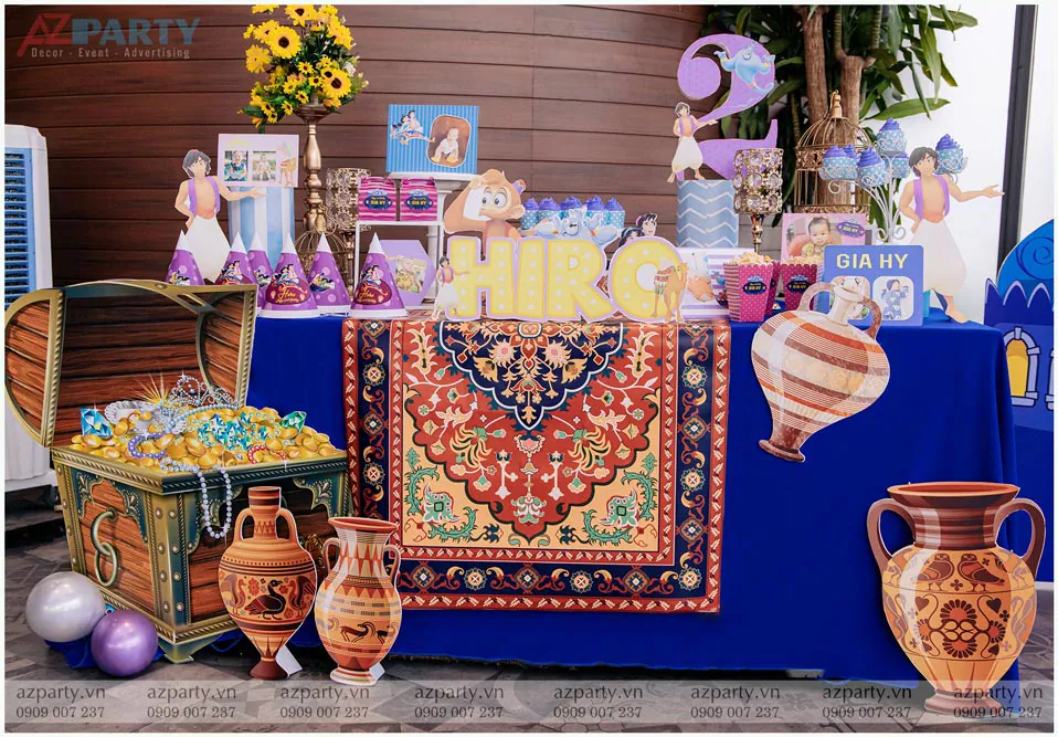 Bàn Gallery tiệc sinh nhật bé Hiro trang trí đậm chất cổ tích Ba Tư với rương kho báu đầy ắp tiền vàng, bình gốm cổ và các nhân vật hoạt hình Aladdin.
