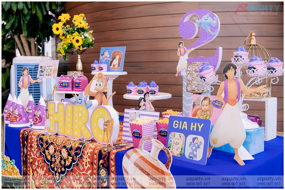 Chi tiết bàn Gallery tiệc sinh nhật bé Gia Hỷ (Hiro) với các khung hình của bé, hoa hướng dương rực rỡ và bánh cupcake trên khay lồng chim nghệ thuật.