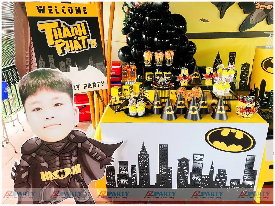 Bàn tiệc ngọt (gallery table) được chuẩn bị chu đáo với nón giấy Batman, bánh ngọt, chai nước và hộp quà trang trí theo tông màu vàng đen chủ đạo.