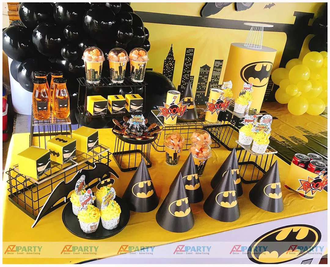 Cận cảnh khay cupcakes kem vàng rực rỡ, bắp rang bơ và các phụ kiện tiệc sinh nhật in logo Batman cực chất.