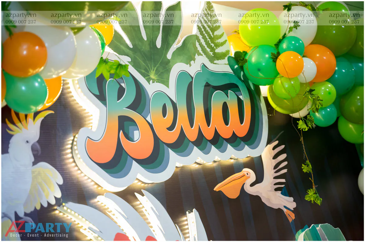 Chi tiết tên bé 'Bella' bằng chữ nổi 3D cách điệu màu cam xanh có đèn LED viền chiếu sáng rực rỡ trên backdrop tiệc sinh nhật.