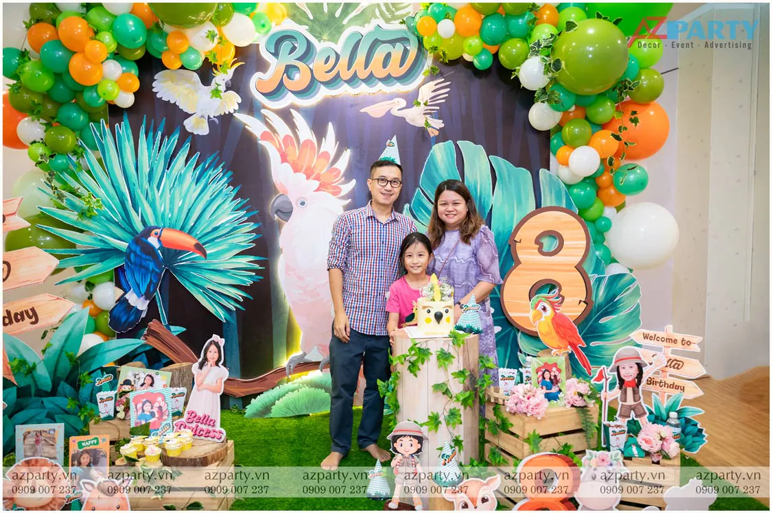 Gia đình bé Bella cười rạng rỡ chụp hình kỷ niệm cùng nhau trước backdrop sinh nhật chủ đề vẹt mào đáng yêu.