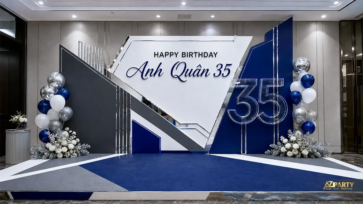 Backdrop sinh nhật Anh Quân 35 tuổi tông xanh navy trắng bạc, phối hình học và bóng ánh kim.