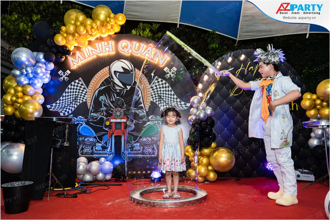 Nghệ sĩ xiếc đang biểu diễn tạo hình bong bóng xà phòng khổng lồ bao trọn bé gái trong quả bóng nước tại sân khấu tiệc sinh nhật bé Minh Quân đầy ảo diệu.