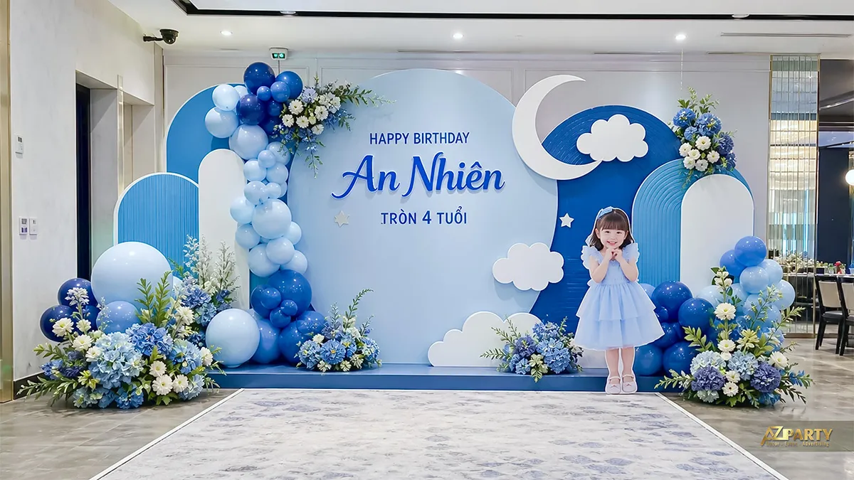 Backdrop xanh trắng mừng sinh nhật An Nhiên tròn 4 tuổi, có trăng khuyết, mây và hoa xanh.