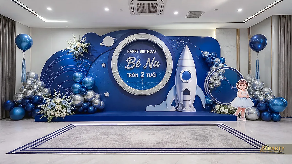 Backdrop xanh chủ đề vũ trụ mừng sinh nhật Bé Na tròn 2 tuổi, có tên lửa và bóng bạc.