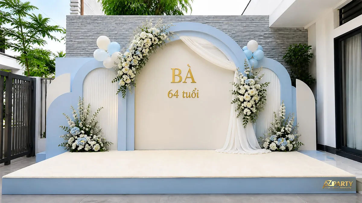 Backdrop sinh nhật người lớn tuổi cho bà 64 tuổi, tông xanh baby kem, phối hoa trắng xanh và rèm vải.