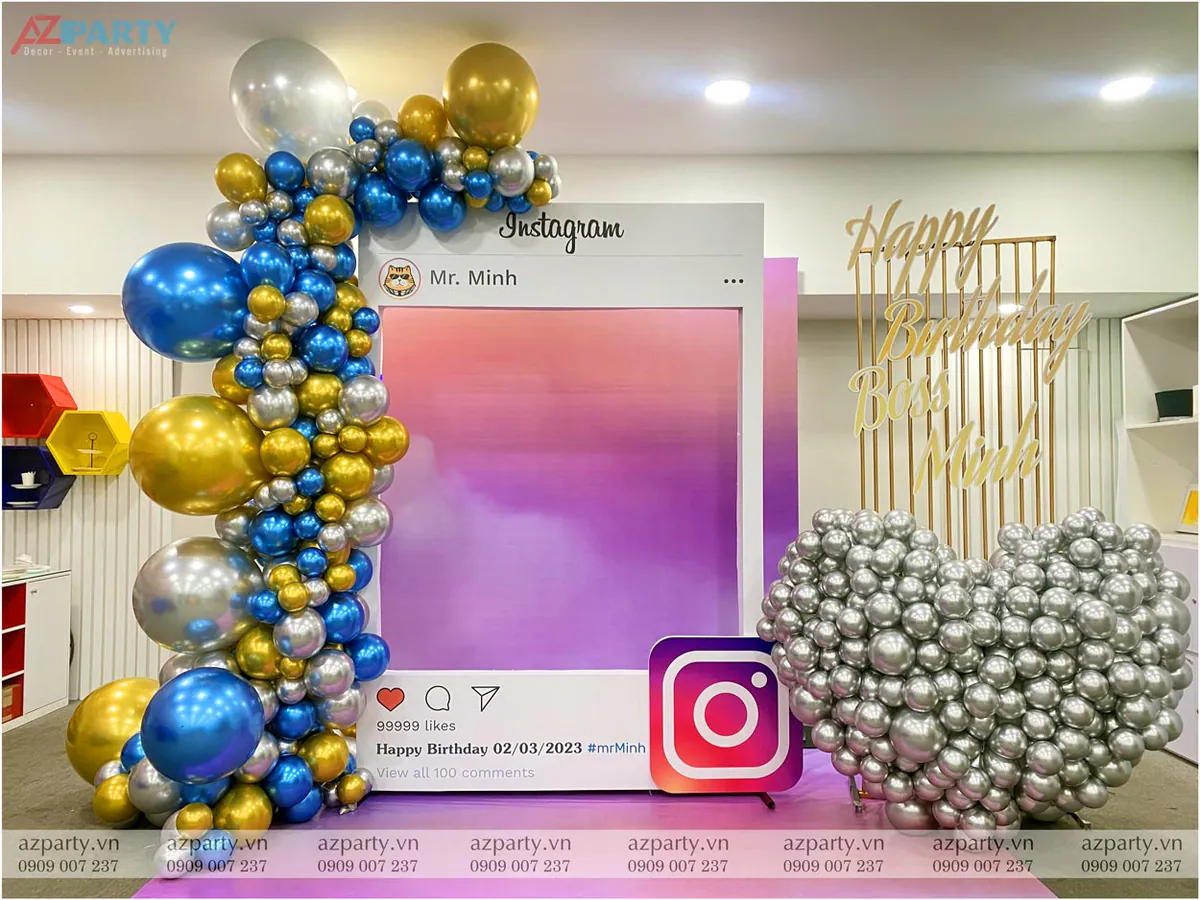 Backdrop chụp ảnh sinh nhật sếp Mr. Minh thiết kế khung giao diện Instagram độc đáo, trang trí cổng bóng bay nghệ thuật xanh dương, vàng và bạc, bên cạnh là cụm bóng hình trái tim màu bạc nổi bật.